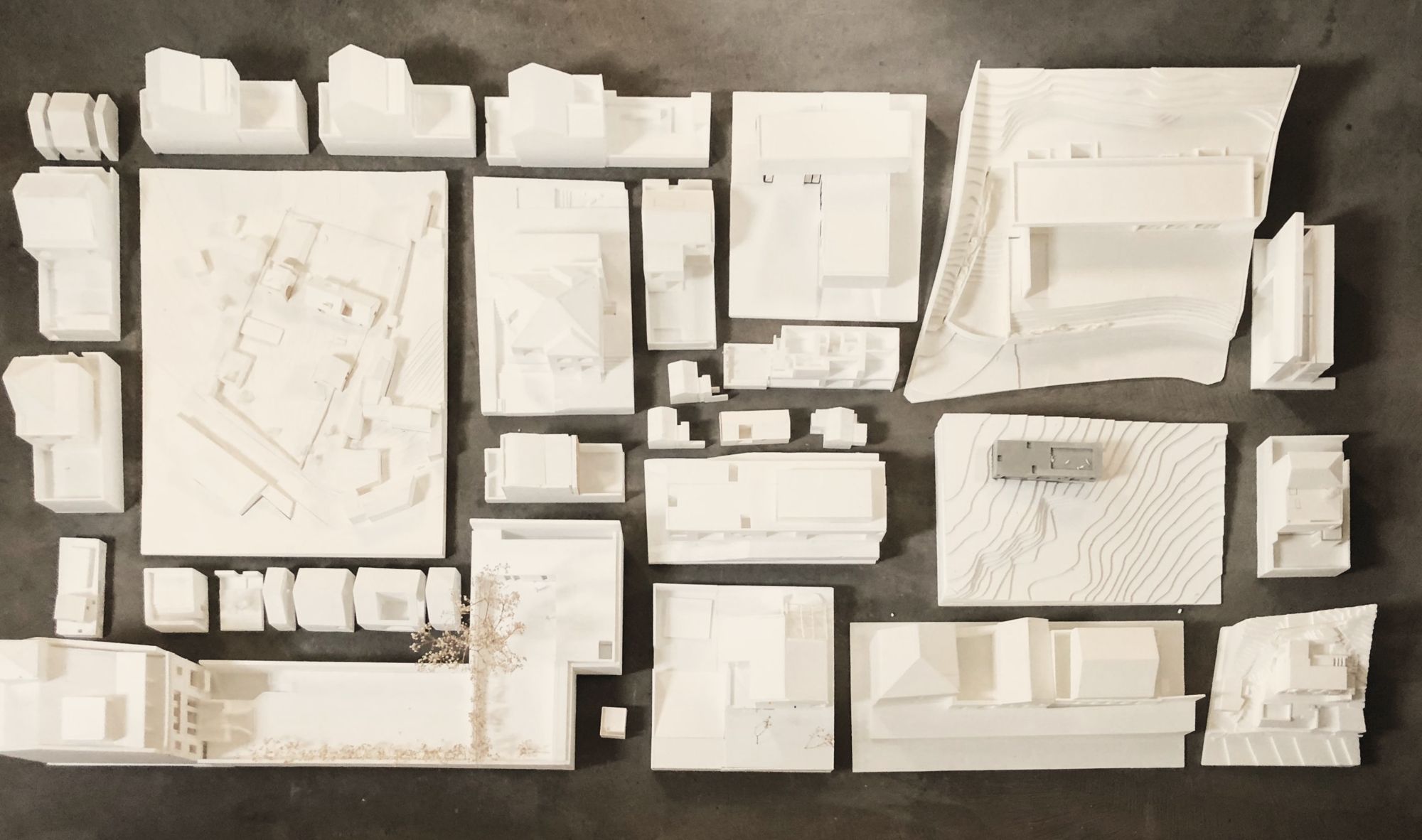Maquetas brancas de vários projetos de arquitetura sobre uma mesa escura